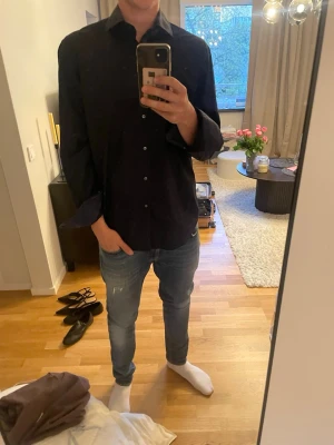 Svart hugoboss skjorta  - Säljer en stilren svart skjorta med klassisk krage och knäppning framtill. Skjortan har lång ärm och en rak passform, perfekt för en clean och enkel look. Passar dig som gillar minimalistisk stil. Det är storlek 43 vilket jag skulle jämföra med L