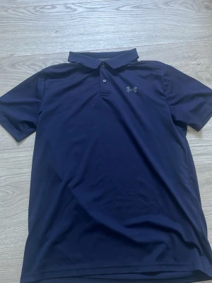 Mörkblå pikétröja från Under Armour - Mörkblå golfpiké tröja från Under Armour. En riktigt schysst piké tröja från Under Armour som passar perfekt vid golfrundan eller på fritiden. Stl YL vilket motsvarar typ 158/164
