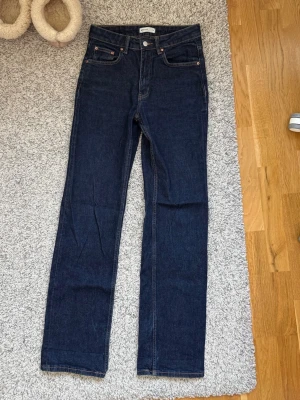 Mörkblå raka jeans - Snygga mörkblå jeans med rak passform och klassisk femficksdesign. Jeansen har silverfärgade nitar och knapp, samt kontrastsömmar. Tillverkade i denim, perfekta till en avslappnad stil.