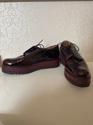 Marko Trend platåskor / creepers i vinröd lack – äkta skinn – strl 40 - Supersnygga platåskor från Marko Trend i mörkt vinröd glansig lackfinish. Tillverkade i äkta skinn med kraftig chunky sula och dekorativa brogue-detaljer som ger en unik och trendig look.  Använda endast en gång och är i nyskick. Sulorna visar minimalt slitage. Perfekta till streetwear, Y2K, goth/grunge eller som statement-skor till vardags.  * Märke: Marko Trend * Storlek: 40 * Material: Äkta skinn * Färg: Vinröd / burgundy * Skick: Nyskick * Kraftig platåsula med bra grepp