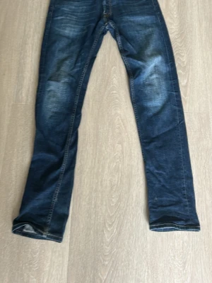 Mörkblå raka jeans med slitningar - Snygga mörkblå jeans med raka ben och diskreta slitningar på låren och knäna. Klassisk femficksmodell med kontrastsömmar och normal midja. Jeansen har en cool tvättad look som passar till det mesta. Storlek 31/34