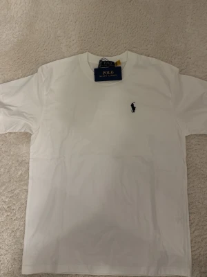 Vit t-shirt från Polo Ralph Lauren - Klassisk vit t-shirt från Polo Ralph Lauren med liten broderad logga på bröstet. T-shirten har rund halsringning och korta ärmar. Perfekt basplagg i mjuk bomull som passar till allt.