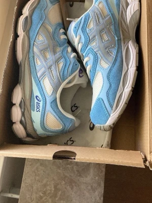 Asics Gel Nyc - Snygga sneakers från Asics i ljusblått och vitt med grå detaljer. Ovandelen är i mesh och mocka för en fräsch och sportig look. Skorna har en tjock, dämpad sula och klassisk Asics-logga på sidan. Perfekta för dig som gillar streetstyle och sportig vibe. Skriv om det finns fler frågor!