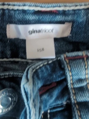 Blå jeans från Gina Tricot - Snygga blå jeans från Gina Tricot i klassisk denim med dragkedja och knapp framtill. Jeansen har synliga sömmar och bälteshällor, perfekt för en trendig och avslappnad look. Materialet är klassisk denim i bomull.