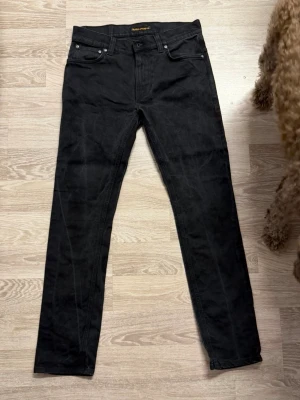 Svarta jeans från Nudie Jeans - Snygga svarta jeans från Nudie Jeans med klassisk femficksmodell och raka ben. Jeansen har diskreta sömmar och en stilren look, perfekta för dig som gillar en enkel och clean stil. Materialet är denim i bomull. Skriv för fler frågor💪🏼