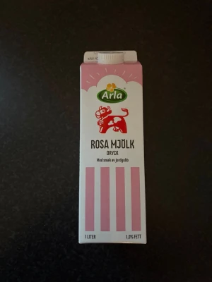 Arla rosa mjölk med jordgubbssmak - En 1-liters förpackning rosa mjölkdryck från Arla med smak av jordgubb. Kartongen är vit och rosa med illustration av en röd ko och rosa ränder. Perfekt till frukost eller mellanmål, och passar även till att göra rosa mannagrynsgröt.