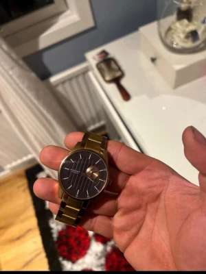 Accent guldfärgad klocka med länkarmband - Snygg guldfärgad klocka från Accent med metallänk och svart urtavla. Urtavlan har tunna vita linjer som markeringar och stilrena visare. Klockan har en klassisk rund form och känns både modern och tidlös.