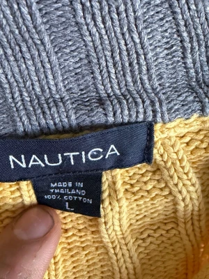 Gul stickad tröja från Nautica - Snygg gul stickad tröja från Nautica i 100% bomull. Tröjan har ett klassiskt kabelstickat mönster och ribbade muddar. Perfekt för dig som gillar en stilren och bekväm look.