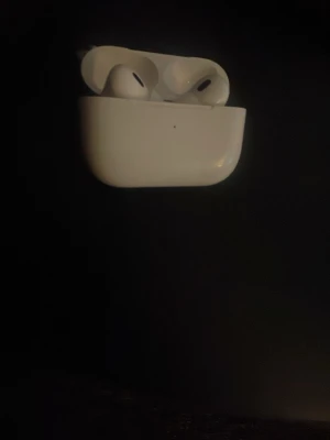 AirPods  - Vita trådlösa hörlurar. Hörlurarna har in-ear design och levereras med tillhörande laddningsfodral. Viss smuts och mindre slitage syns på hörlurarna och etuiet, men överlag i bruksskick. Perfekt för musik och samtal på språng. 