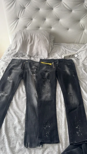 Svarta s jeans med dragkedjedetalj - Säljer ett par svarta  jeans från Dsquared2 med slitningar, färgstänk och en stor silverfärgad dragkedja framtill. Jeansen har en cool, tvättad look och detaljer som ger en edgy streetstyle-vibe. Perfekta för dig som gillar statement-plagg.
