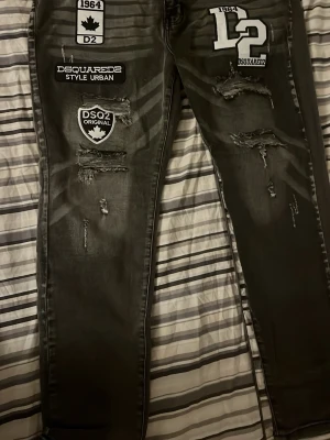 Svarta Dsquared2 jeans med patches - Snygga svarta jeans från Dsquared2 med flera coola patches och slitningar framtill. Jeansen har smal passform och detaljer som DSQ2-logga, kanadensiskt lönnlöv och texttryck. Perfekta för en streetwear-look.