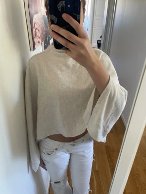 Beige poncho topp med vida ärmar ginatricot  - Trendig poncho topp i beige med vida, långa ärmar och hög hals. Tunt och mjukt material som ger en avslappnad vibe. Perfekt att styla med jeans eller kjol för en cool look.