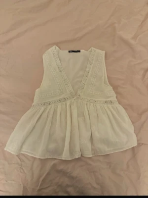 Vit ärmlös blus med spetsdetaljer - Supersöt vit blus från Zara med djup v-ringning och fina spetsdetaljer längs kanterna. 