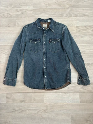 Levi's jeansskjorta Barstow Western - Klassisk mörkblå jeansskjorta från Levi's Barstow Western med tryckknappar och två bröstfickor. Skjortan har lång ärm och kontrastsömmar som ger en snygg vintagekänsla. Perfekt för dig som gillar en tidlös och avslappnad stil.