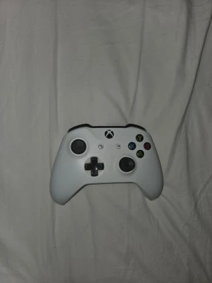 Vit Xbox One handkontroll - Säljer en vit Xbox One handkontroll med klassisk design, svarta detaljer och färgade knappar. Ergonomisk form och tillverkad i plast, perfekt för gaming på Xbox eller PC. Det är dessutom ingen stickdrift eller något.