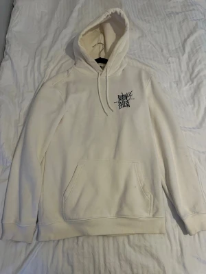 Vit hoodie från H&M med tryck - Säljer en vit hoodie från H&M i regular fit med svart tryck på bröstet. Hoodien har huva med dragsko och en stor magficka framtill. Perfekt för dig som gillar enkel och stilren streetwear. Materialet är mjukt och skönt bomullstyg.