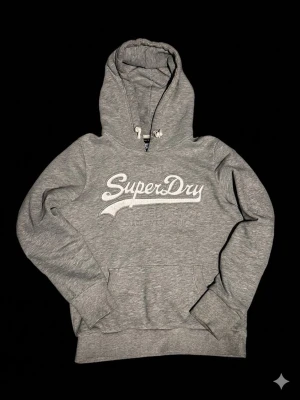 Grå hoodie från Superdry - Grå hoodie från superdry. Knappt använd med snygg logga på framsidan. På tecken på armen och bröstet. Två snören som ger en avslappnade look och används till spänning av luvan. En perfekt every day hoodie. Priset går att diskutera vid snabb affär. Hör av er vid funderingar😁