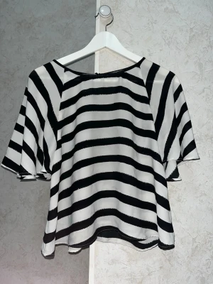 Randig blus från Kappahl  - Säljer en luftig blus från Kappahl i storlek XS. Blusen har svartvita, zebra ränder och vida, korta ärmar. Lite genomskinlig. Materialet känns lätt och flowy, perfekt för en chill look. Rund halsringning och avslappnad passform.
