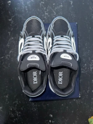 Nike sneakers - Snygga svarta sneakers från Nike med vita och grå detaljer. Skorna har tydlig nike logga på plösen och insidan, samt coola kontrastsömmar och snörning. Ovandelen är i mesh och syntetmaterial för en modern look.