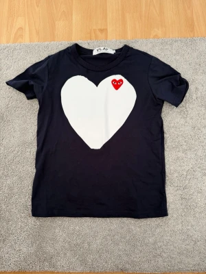 Cdg T-shirt - Säljer en stilren CDG PLAY t-shirt i mörkblå färg med stort vitt hjärta och klassiska röda PLAY-loggan. Väldigt clean och populär modell som passar till allt. Helt oanvänd endast testad.