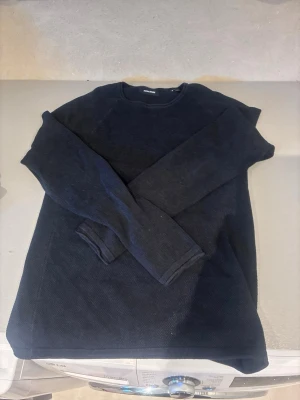 Svart långärmad tröja från Jack & Jones - En stilren svart långärmad tröja från Jack & Jones. Tröjan har rund halsringning och är tillverkad i ett mjukt, stickat material som passar perfekt till lager-på-lager. Enkel och clean design som funkar till det mesta.