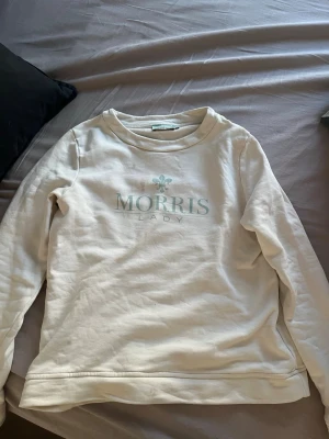 Vit sweatshirt från Morris Lady - Snygg vit sweatshirt från Morris Lady med tryckt logga framtill i ljusgrönt. Tröjan har rund halsringning och långa ärmar. Perfekt för en avslappnad och stilren look. Tillverkad i mjukt bomullsmaterial som känns skönt mot huden.