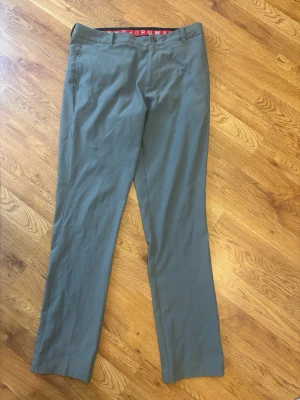 Gråa golfbyxor från Puma Strl 32/34 - Snygga grå chinos från Puma med rak passform och klassisk design. Byxorna har bälteshällor, två sidofickor fram och två passpoalfickor bak. Perfekta för en stilren och avslappnad look. Materialet känns mjukt och följsamt.