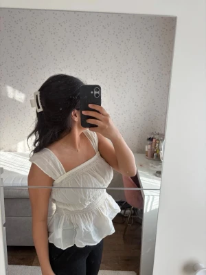 Topp med volang - Söt vit linnetopp med breda axelband och volang nedtill. Toppen har smock i midjan och en luftig, flowy passform. Har använt några få gånger bara. Nypris 249kr