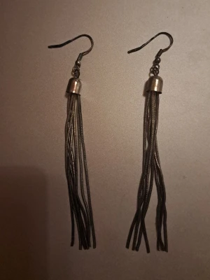 Silvriga långa tofsörhängen - Säljer ett par coola örhängen i silver samt svart med långa, tunna kedjor som hänger i tofsar. De har en enkel krok och ger en snygg statement-look. Perfekta för dig som gillar att sticka ut med accessoarer.