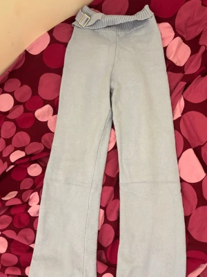 Ljusblå ribbade leggings med spänne - Supersnygga ljusblå leggings i ribbat stickat material med ett dekorativt guldfärgat spänne i midjan. Midjan är lite insydd i bak (bild 6). Det här är ett sätt, men säljer bara byxorna eftersom dom är för små.