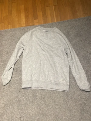 Ljusgrå sweatshirt från  - En stilren ljusgrå sweatshirt från Samsoe Samsoe med rund halsringning och ribbade muddar vid ärmslut och nederkant. Perfekt basic-plagg att matcha med jeans eller kjol. Mjuk bomullskänsla och relaxed fit.