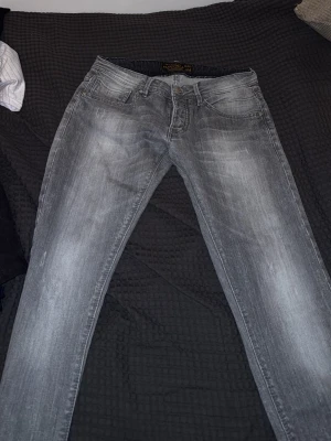 Grå slitna jeans från Tiger of Sweden - Säljer ett par grå jeans från Tiger of Sweden med snyggt sliten tvätt och smal passform. Klassisk femficksmodell med dragkedja och knapp. Perfekta för dig som gillar en modern och avslappnad stil.