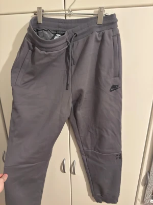 Gråa mjukisbyxor - Säljer ett par gråa mjukisbyxo med ribbade muddar. Byxorna har två sidofickor och Nike-logga på vänster ben. Tillverkade i mjukt material som passar perfekt för chill dagar. Snygg, enkel design med tryckdetaljer på benen. OBS. TAGG SÄGER XXL MEN PASSAR M-L. 