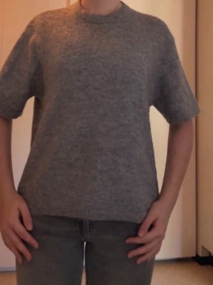 Grå stickad tröja från Gina Tricot - Grå stickad tröja från Gina Tricot i mjuk ullblandning. Tröjan har korta ärmar, rund halsringning och ribbade kanter. Väldigt härligt material som är både snyggt och bekvämt! I mycket bra skick och använd fåtal gånger!💗