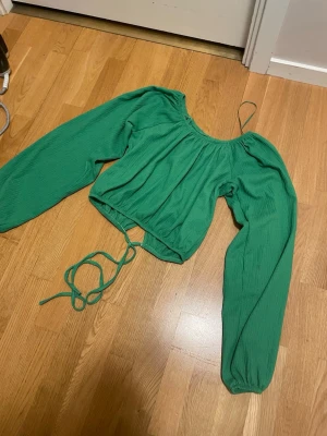 Grön croppad blus med snörning - Trendig grön blus med långa puffärmar och croppad passform. Toppen har rundad halsringning och snörning i midjan för en justerbar look. Perfekt för dig som vill sticka ut med färg och stil. Ryggen ska egentligen vara öppen men har sytt ihop det kan säkert sys upp ifall man vill ha det öppet. Färgen syns bättre på sista bilden