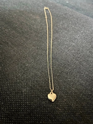 Guldfynd halsband med hjärthänge - Säljer ett elegant halsband i guld från Guldfynd med ett litet hjärthänge. Kedjan är tunn och smidig, perfekt för dig som gillar stilrena smycken. Kommer i original ask från Guldfynd.