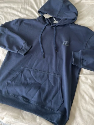 blå hoodie  från CD - Snygg mörkblå hoodie från CD med broderad logga på bröstet. Klassisk känguruficka framtill, ribbade muddar och justerbar huva med dragsko. Tillverkad i mjuk bomullsblandning för en skön och avslappnad look.