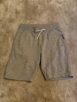 Gant shorts - Mysiga grå sweatshorts med resårmidja och vit snörning i midjan. Två sidofickor framtill och liten broderad logga på vänster sida. Perfekta för chill eller träning.