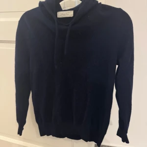 Mörkblå kashmir hoodie från sayless - Mysig mörkblå hoodie från sayless i lyxig kashmir. Tröjan har huva med snörning och långa ärmar, perfekt för dig som gillar en stilren och enkel look. Passformen är normal och materialet är supermjukt och värmande.