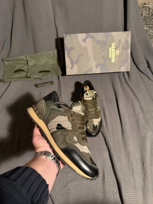 Valentino rockrunner  - Snygga sneakers från Valentino med camouflage-mönster i olika nyanser av grönt, beige och svart. Skorna har detaljer i mocka och mesh, svarta partier vid tån och hälen samt en beige sula. Klassisk låg modell med gröna skosnören och logga på plösen.