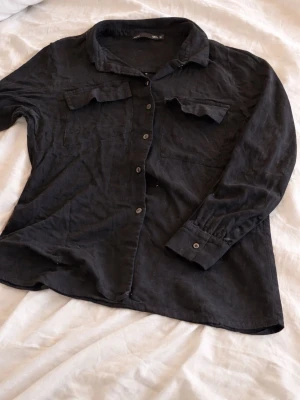 Svart manchester skjorta med fickor - Säljer en svart långärmad skjorta från Lager 157 i mjuk manchester. Skjortan har två bröstfickor med lock, klassisk krage och knappar framtill. Perfekt för en avslappnad och stilren look.