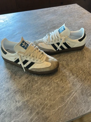 Adidas samba - Klassiska Adidas Samba sneakers i vitt läder med svarta ränder och brun sula. Använda väldigt fåtal gånger. Skriv vid minsta fundering!