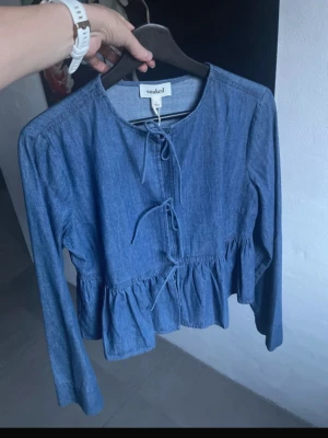 Blå jeansblus från Soaked - Trendig blå jeansblus från Soaked med volang nedtill och knytband framtill. Blusen har rund halsringning och långa ärmar. Tillverkad i mjukt denimtyg som ger en avslappnad men ändå stilsäker look.Strl M men passar även xs/s. Köpt för 1000kr. Slutsåld💕