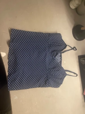 Mörkblå prickigt nattlinne med spets - Sött nattlinne i mörkblått med vita små prickar, tunna axelband och spetsdetaljer vid urringningen. Liten rosett framtill för extra detalj. Mjukt och lätt material som känns skönt mot huden. Perfekt för mysiga kvällar hemma.