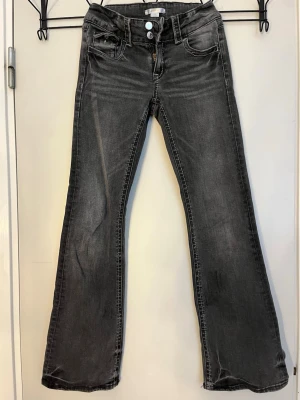 Svarta bootcut jeans med slitningar - Snygga svarta bootcut jeans. Jeansen har klassisk femficksmodell, dubbla knappar i midjan och utsvängda ben. Perfekta för en avslappnad och trendig look.