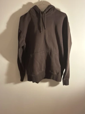 Mörkbrun basic hoodie med ficka från Jack and Jones  - En enkel och stilren mörkbrun hoodie med huva och dragsnören. Hoodien har en stor känguruficka framtill och ribbade muddar vid ärmslut och nederkant. Perfekt för en avslappnad look och passar till det mesta.