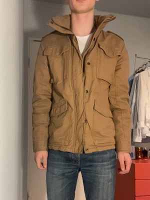 Field jacket - En brun fieldjacka från L.O.G.G och hm. Nästan nyskick. Fodrad och med många snygga detaljer. En replika av militära m65. (Jag är 175 cm) 