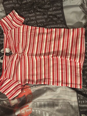 Rödvit randig ribbad topp H&M - Säljer en ribbad topp från Divided med röda och vita ränder. Toppen har korta ärmar, hög hals och är figurnära i modellen. Perfekt för dig som gillar färgglada och bekväma plagg med lite retrovibe.