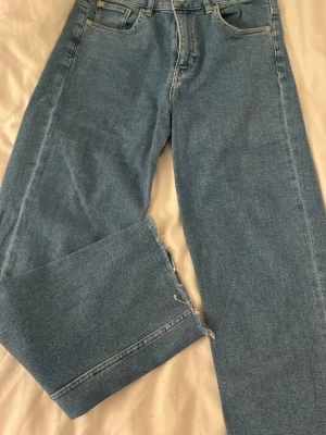 Blå raka jeans med kant - Ett par ljusblå raka jeans i klassisk denim med rå, fransig kant nedtill på benen.