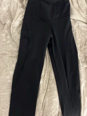 Svarta leggings med hög midja - Snygga svarta leggings med hög midja och praktiska sidofickor. Tillverkade i stretchigt material som sitter skönt och formar sig efter kroppen. Perfekta för träning eller chill. Inga synliga loggor eller märken.